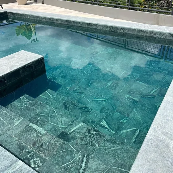 Piscina revestida em pedra natural com deck de madeira