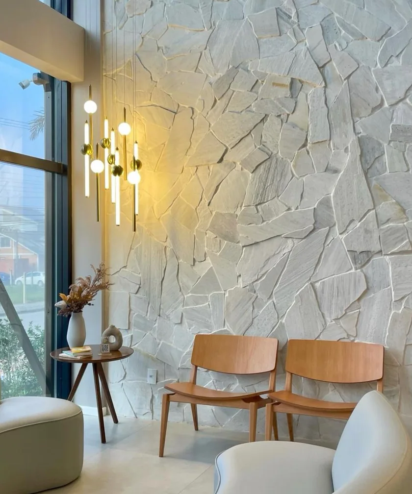 Sala de espera com parede em pedra natural branca e luminária dourada